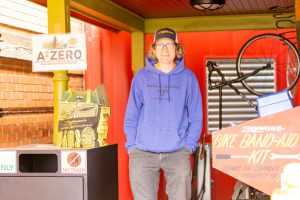 a photo of Rodger Bowser standing on the front porch at the Deli next to a bike rack