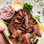An Instagram photo of sliced corned beef and sliced Swiss cheese on a bed of lettuce with small cups of coleslaw and Russian dressing on the side, with a sheet of Zingerman's Deli paper under everything.