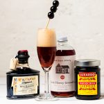Making a Mean Mocktail: A Zingerman’s Crash Course A photo of a bottle of La Vecchia Dispensa Balsamic Vinegar, a bottle of PinkHouse Dark Cherry Grenadine, and a jar of Luxardo Maraschino Cherries along with a champagne flute filled with a balsamic vinegar spritzer topped with a toothpick of maraschino cherries.