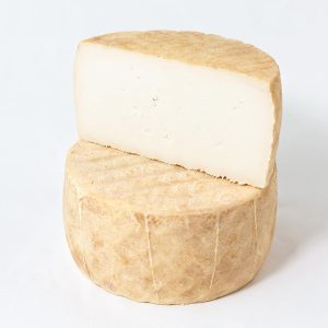 A photo of one whole wheel of Gofio goat cheese, with a half wheel stacked on top. The cheese has a very thin pale rind, with a white interior that has a thick and solid paste.