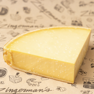 A quarter of a wheel of Dutch Gouda cheese on a sheet of Deli parchment paper.